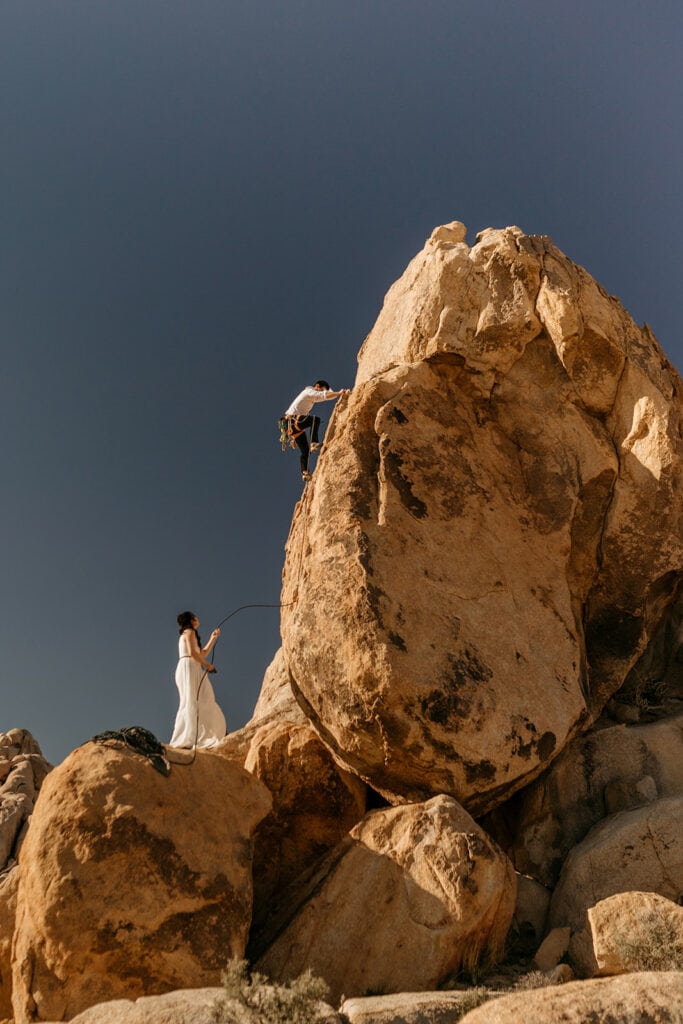 A groom makes his way up a rock climbing in joshua tree.