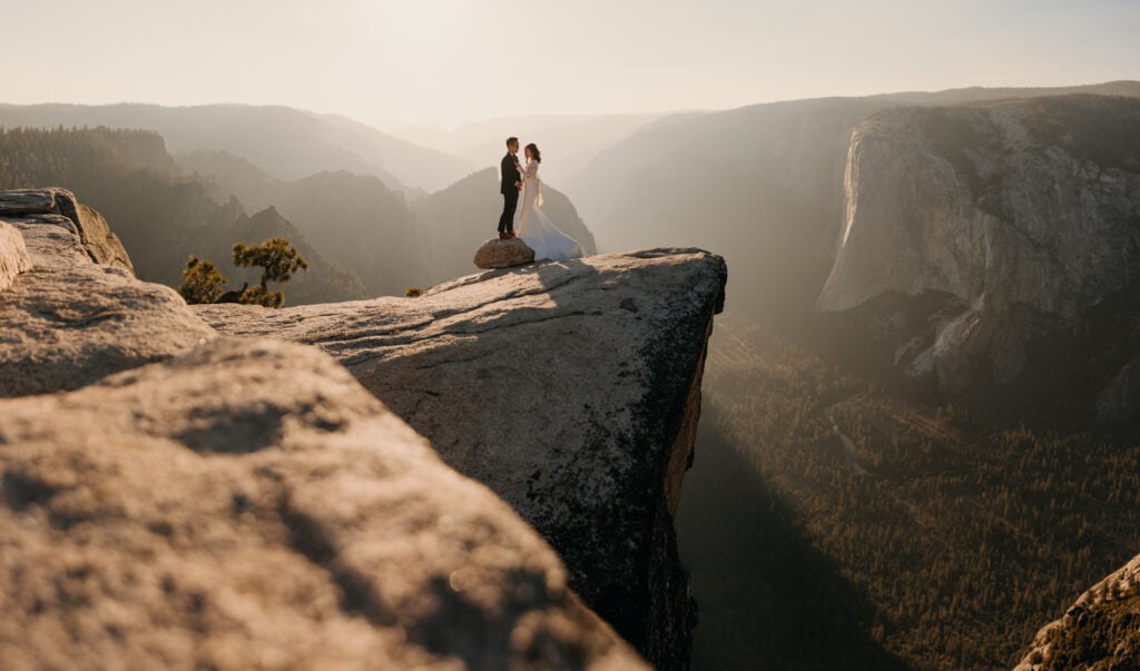A couple stands on a cliff as the sun sets behind them as they emotionally share their vows.