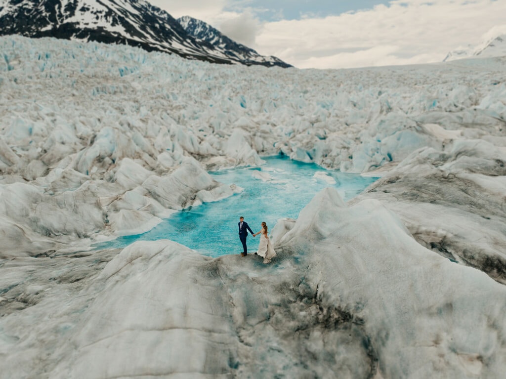 A bride and groom walk along a glacier pool on top of a glacier in Palmer, Alaska.