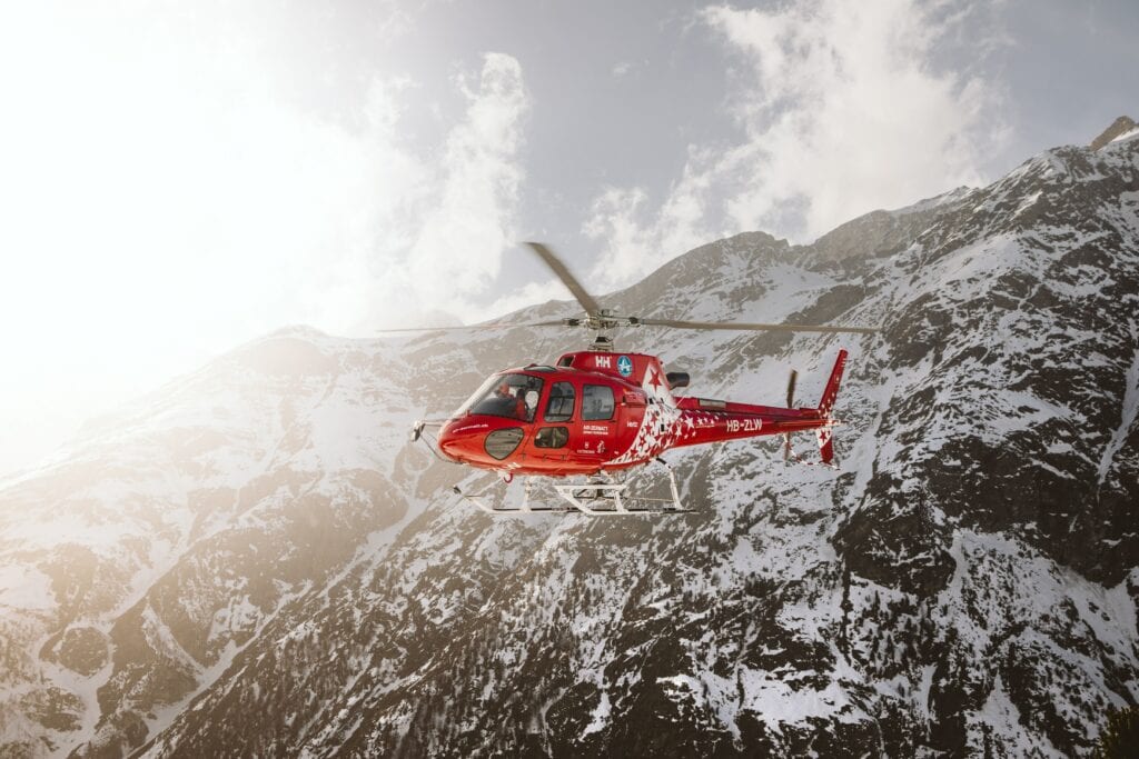 A helicopter flying past a snow mountain on a sunny day in Alaska.