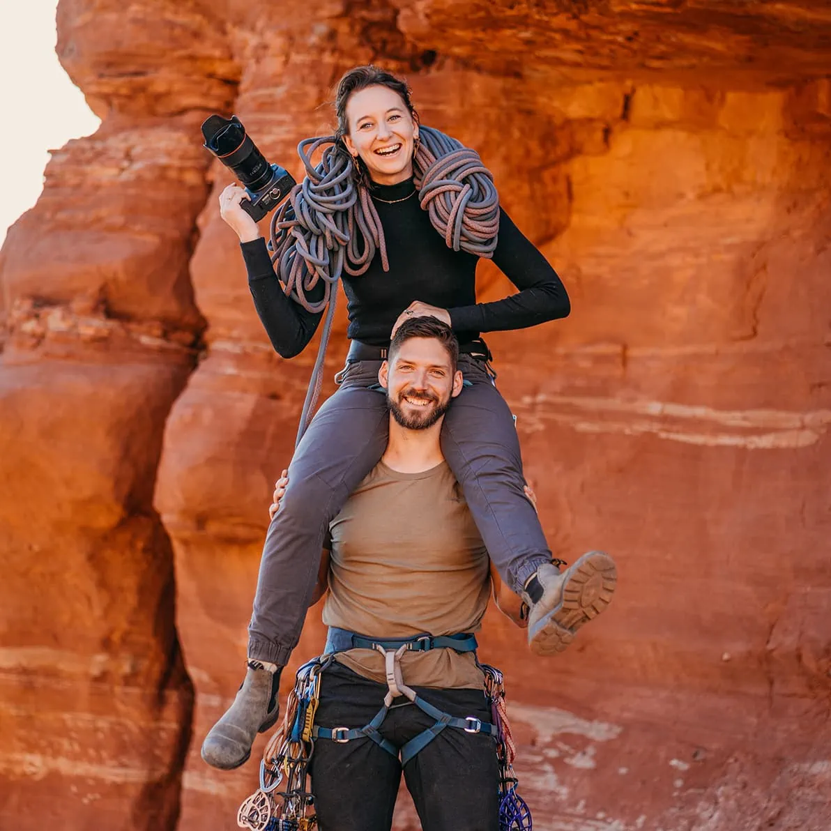 A couple poses for a headshot with their camera and climbing gear.