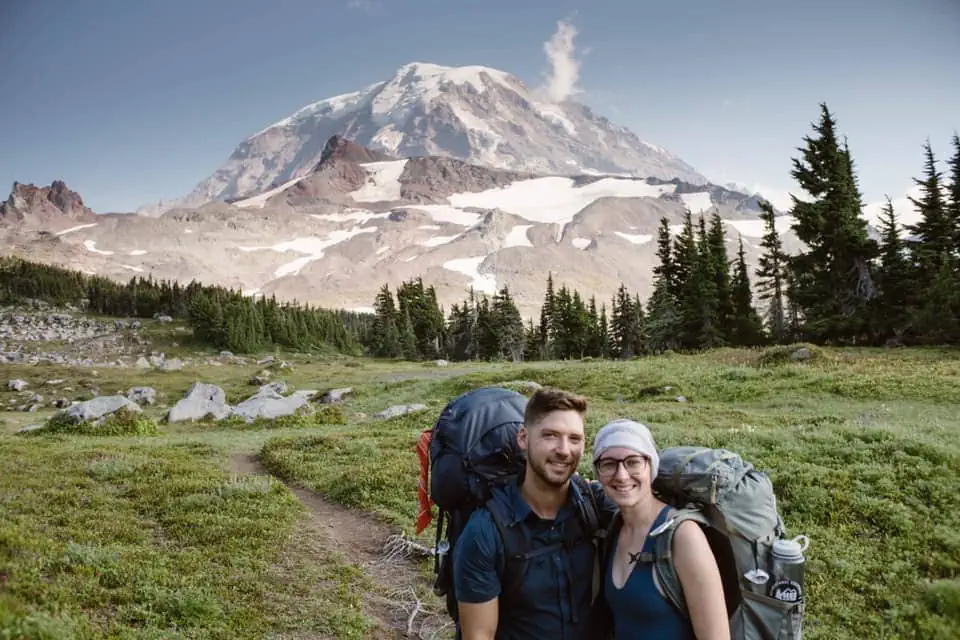 A backpacking couple smiles for a photo n the trial with their packs in Mount Rainier National Park. 