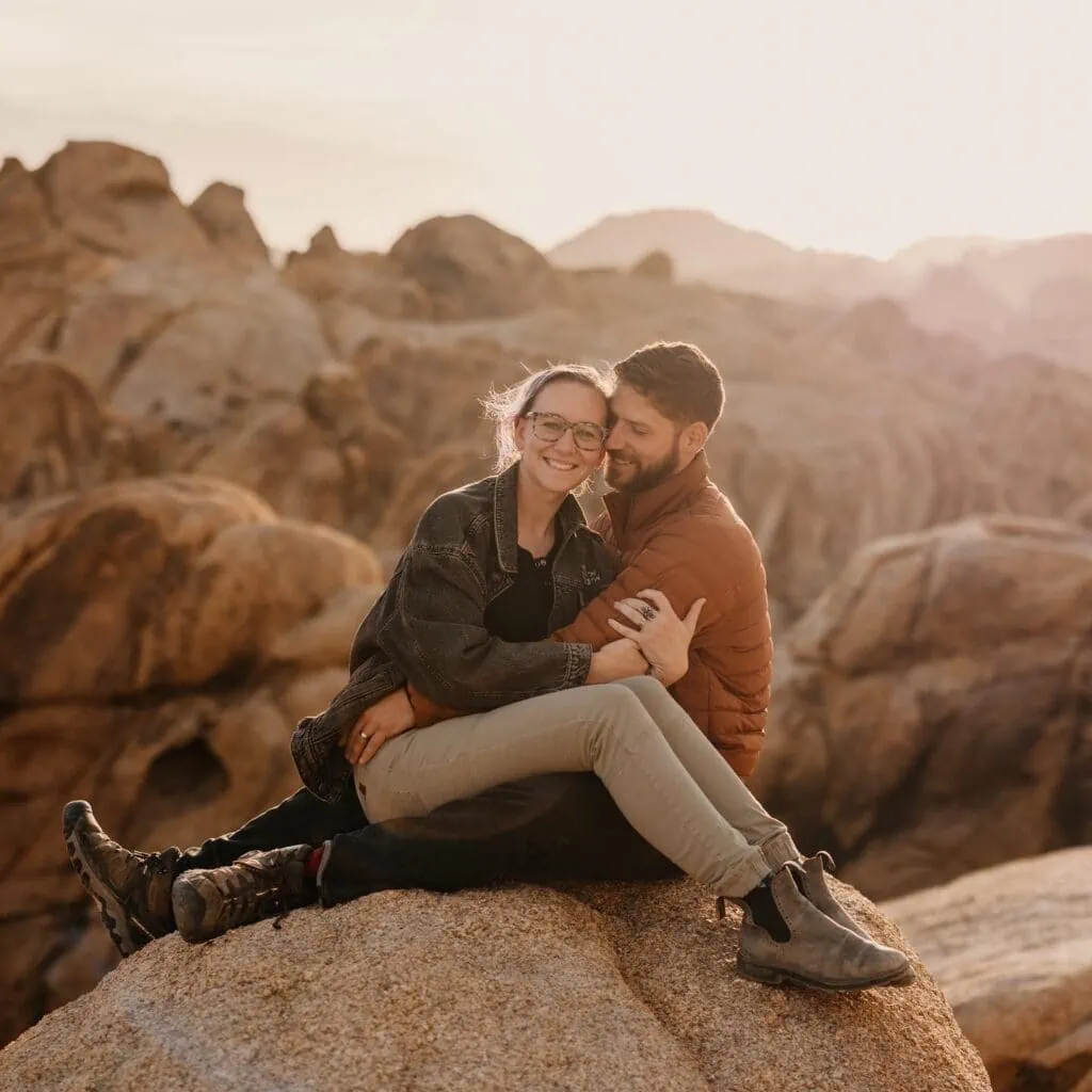 A man and woman sit together among the white granite of Joshua Tree at sunset.