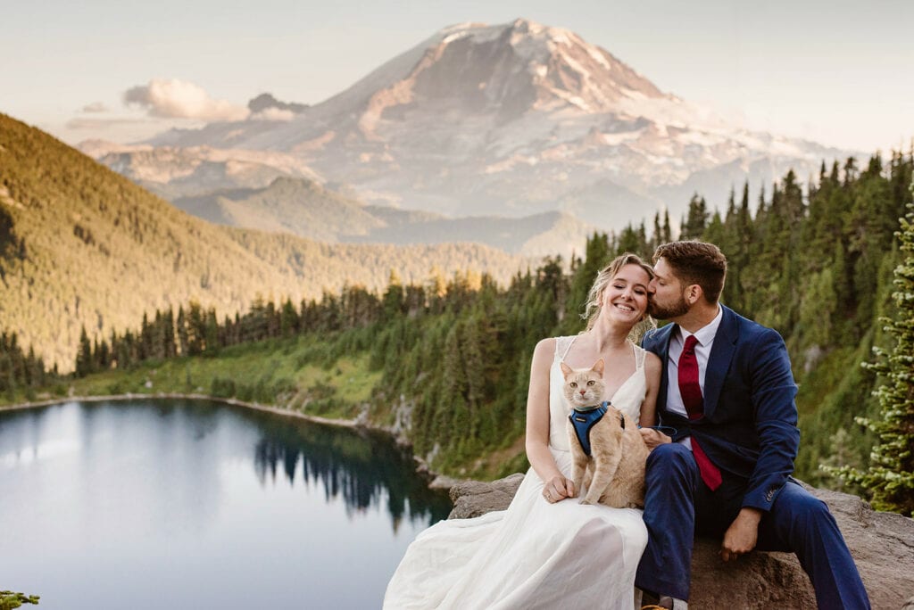 A couple and their cat pose for a photo at their wedding with mt rainier in the background.
