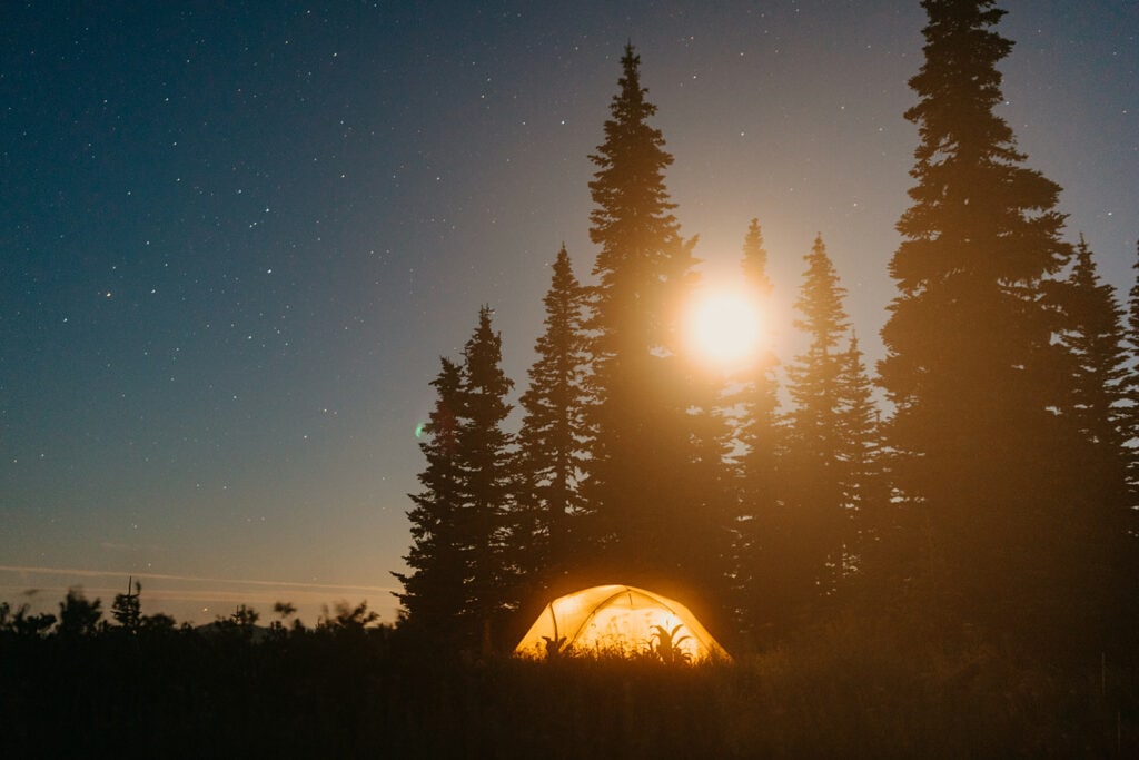 A tent under the stars while the moon comes up over the trees. 