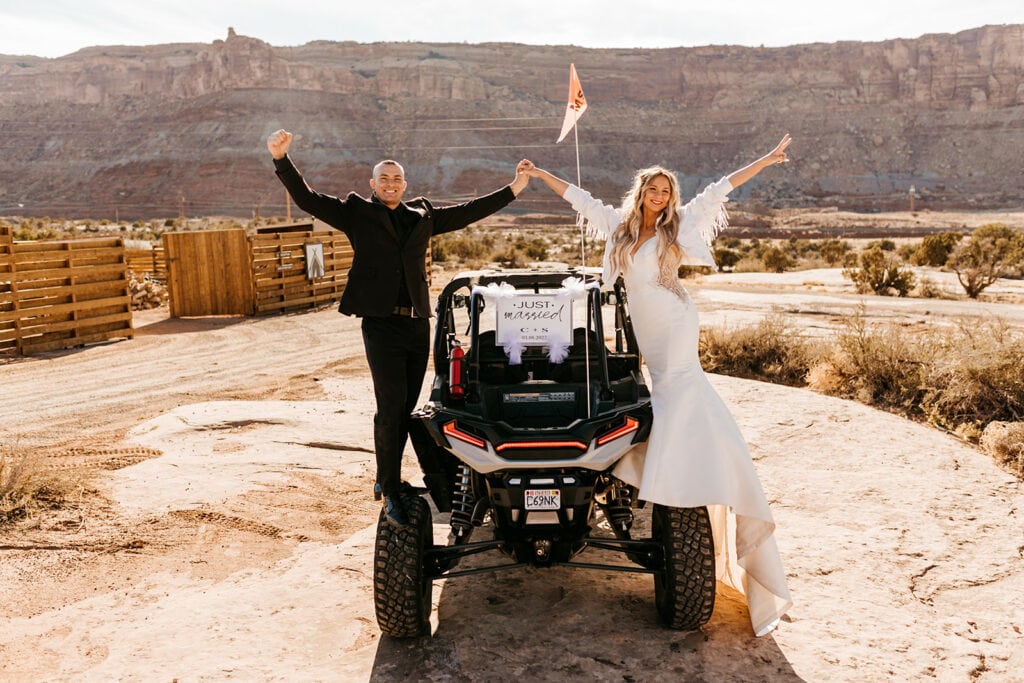 A bride and groom stand on the back of their ATV with their just married sign! 