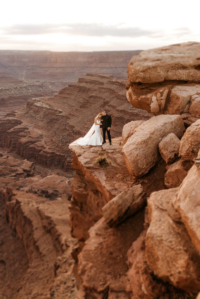 A bride and groom embrace each other closely on the side of a cliff in Moab.
