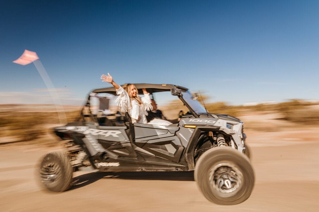 A bride waves her hand out of the ATV her groom is driving. 