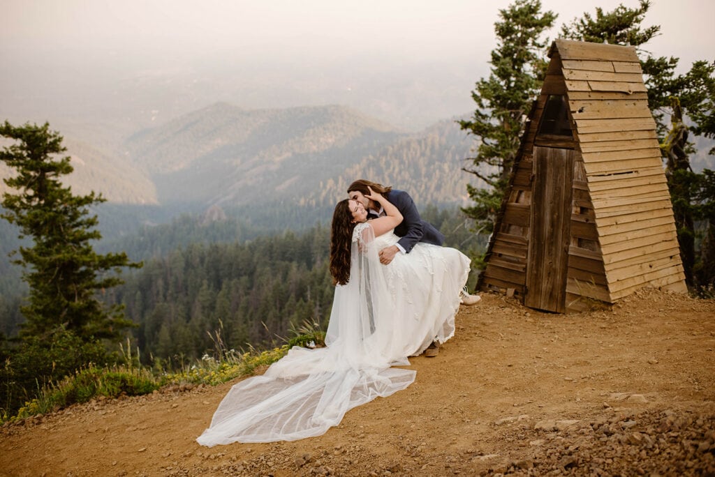 A groom dip kisses his bride in the mountains.