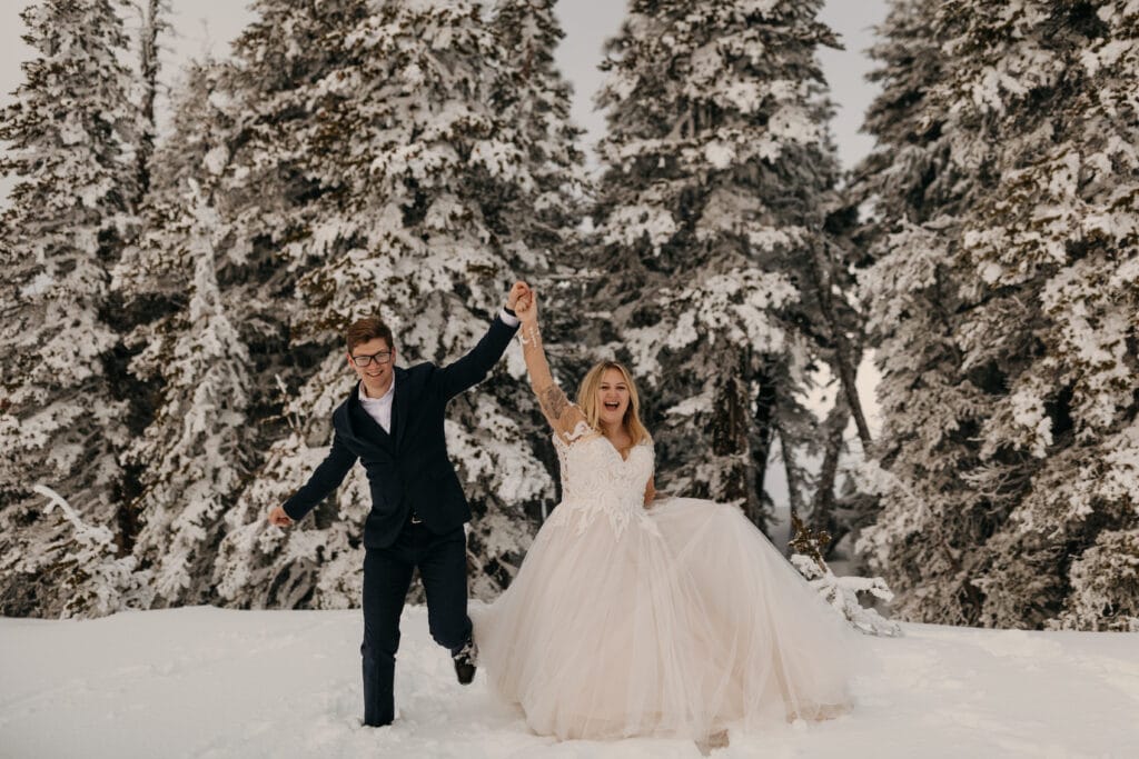 The bride and groom hold hands together and celebrate after a ceremony in the mountains during the winter