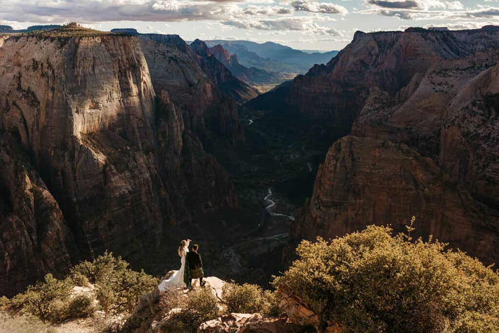The bride and groom look out over the view of Zion National Park while standing over a thousand feet up at the top of a cliff