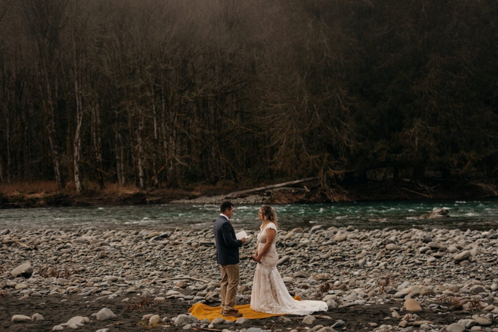 A couple shares vows by a river on a winter day in Washington.