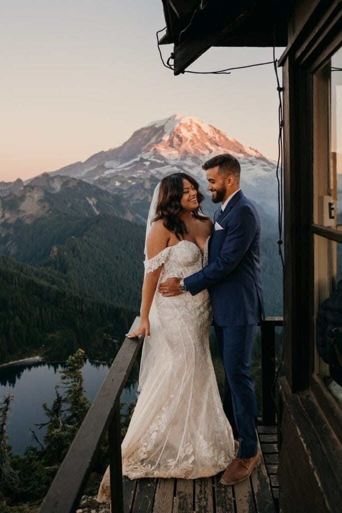A bride and groom stand together on a firetower overlooking Mt. Rainier.