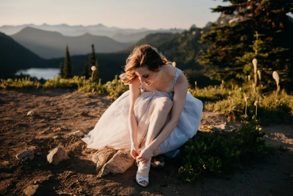 A bride puts her shoe on the side of the trail.