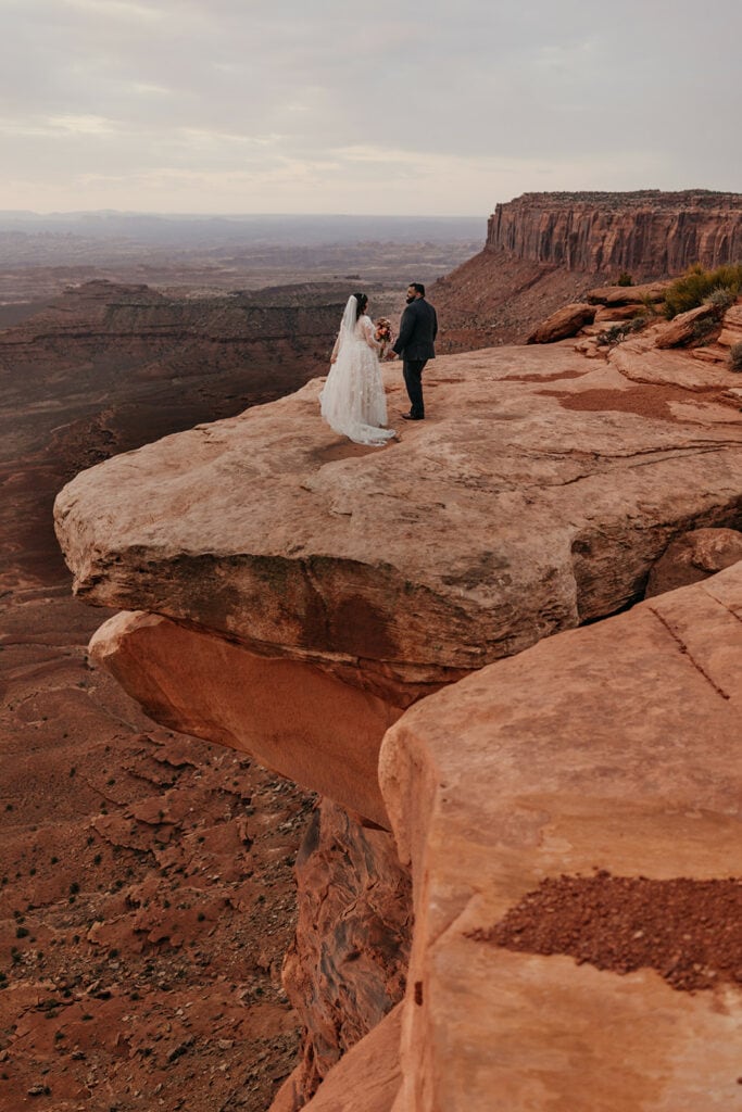A couple stands on a huge rock ledge in Canyonlands.