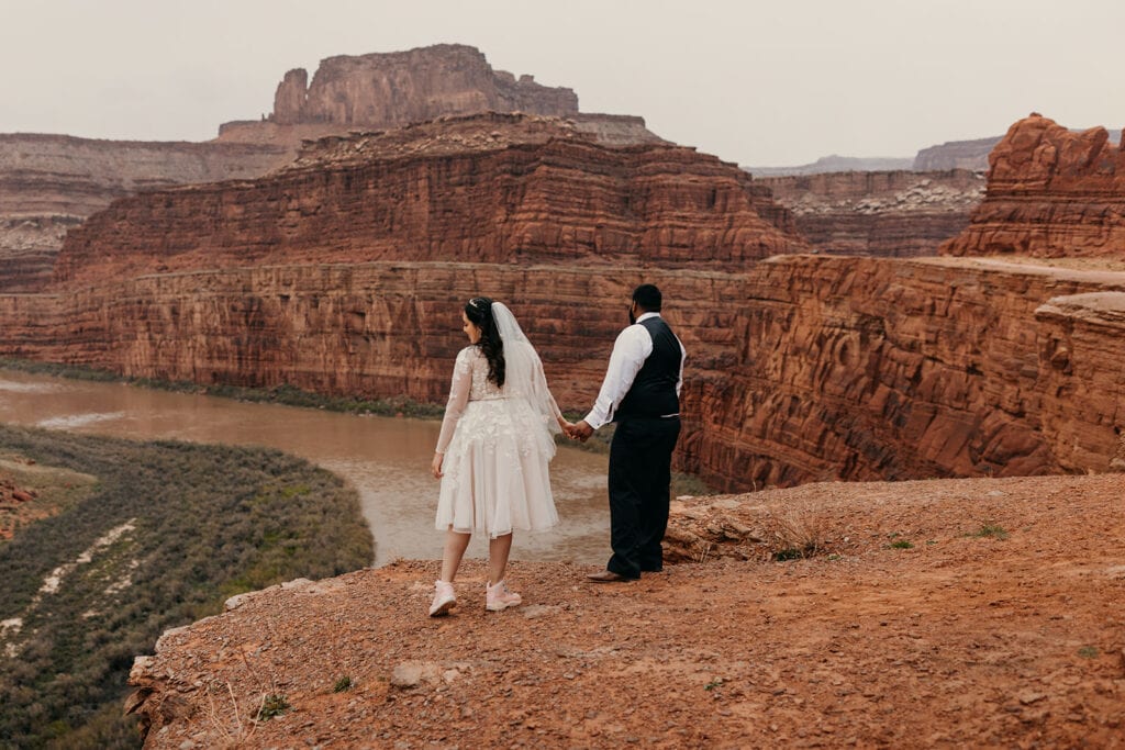 A bride looks over the edge of a canyon towards the Colorado River.