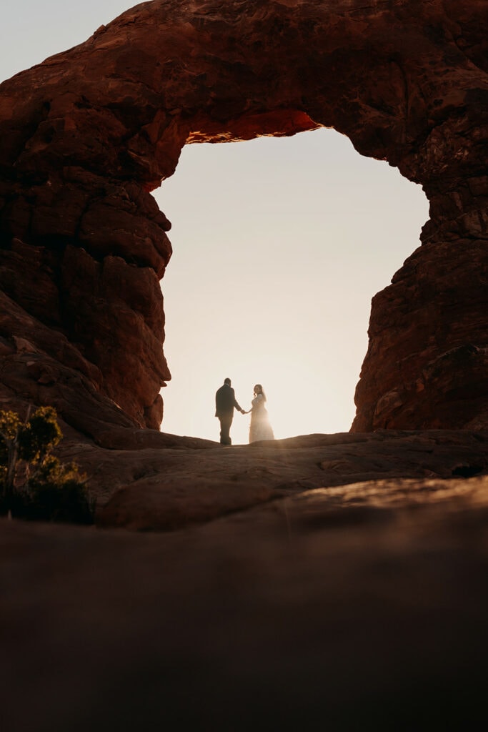 a bride and groom stand together under turret arch in arches national park