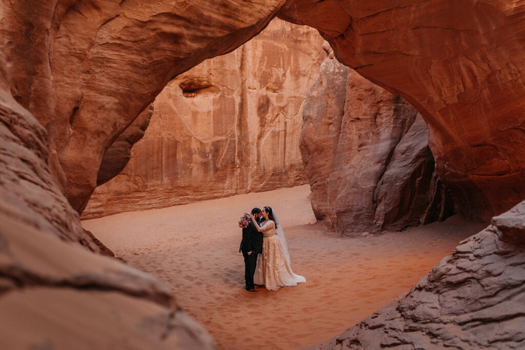 The couple stands under Sand Dune Arch together.