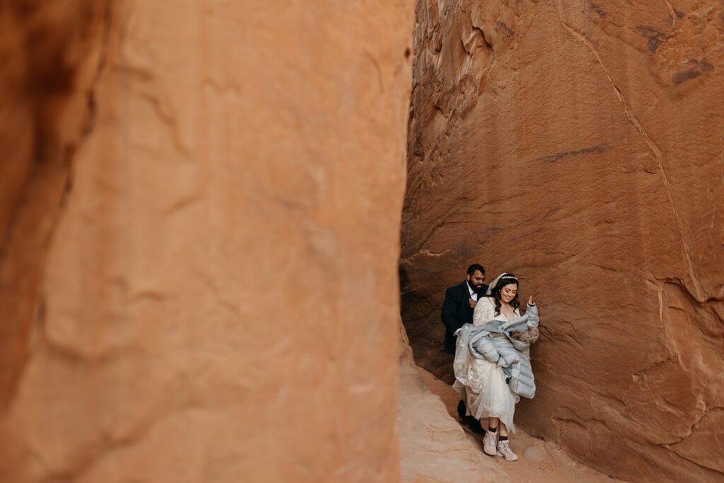 A bride and groom walk together in Arches national park near Sand dune arch