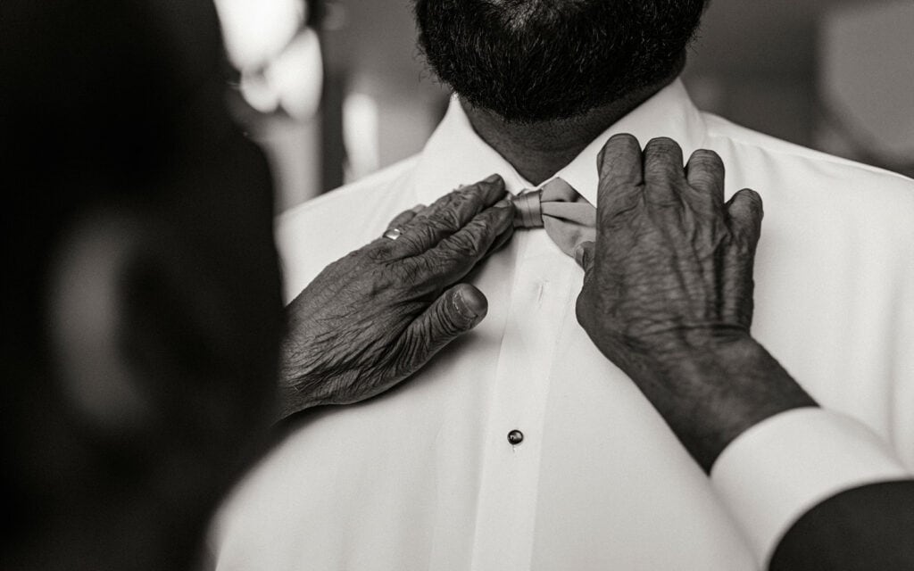 A detail of the groom's father's hands helping him with his bowtie.