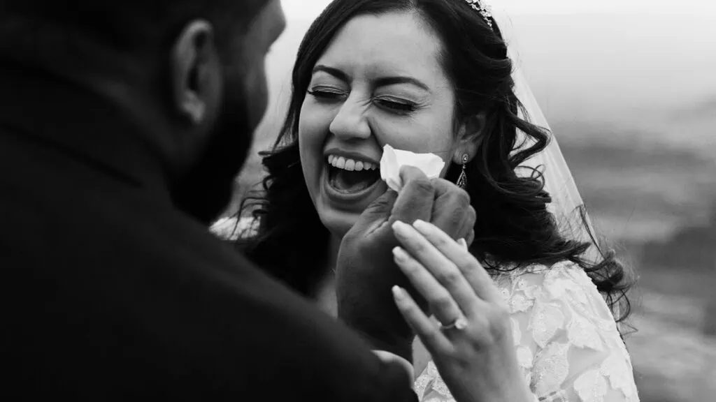 A groom wipes the brides tears away as she laughs.