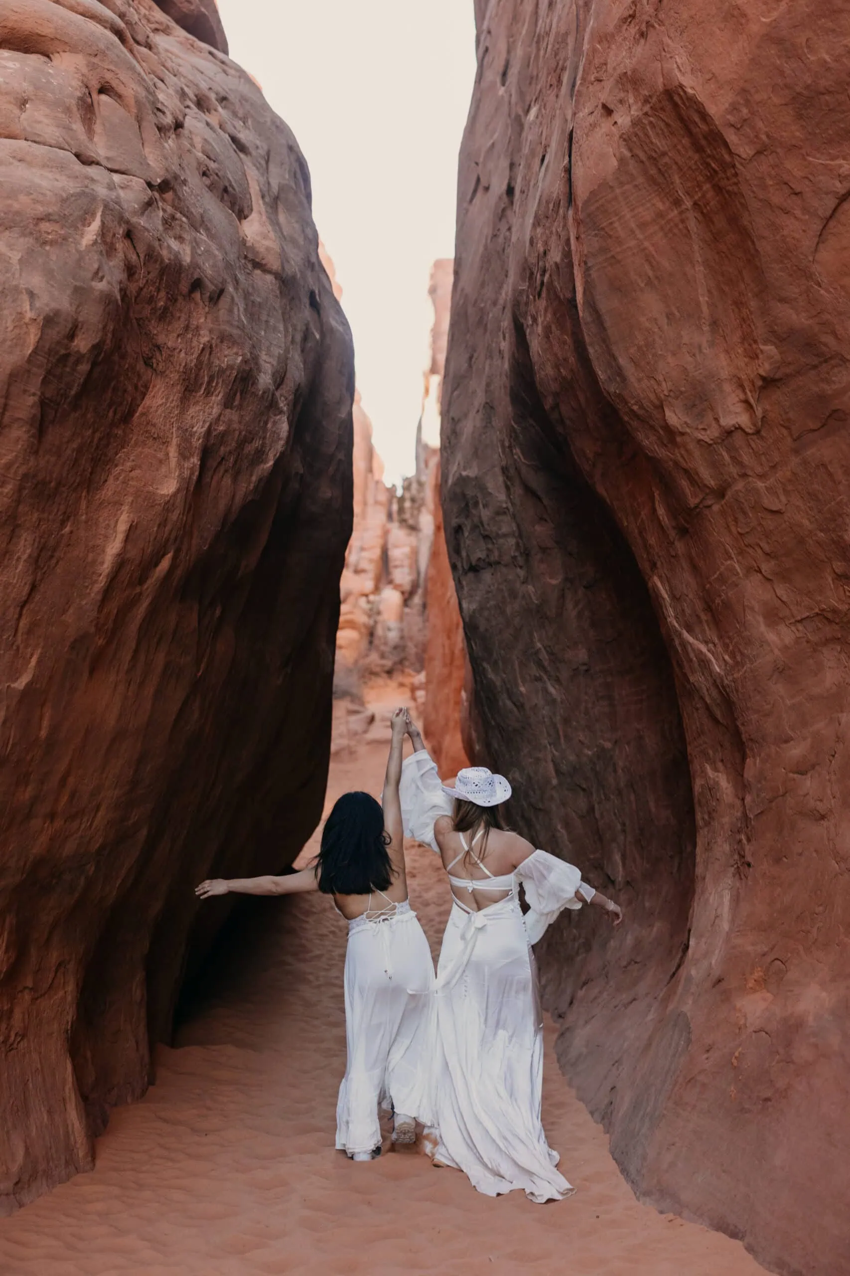 Two brides walk through the sand together in Arches National Park.