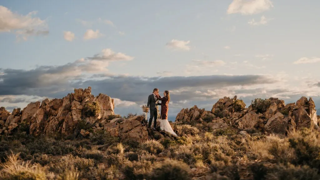 A portrait of the couple standing on rocks in the sunlight of the desert.