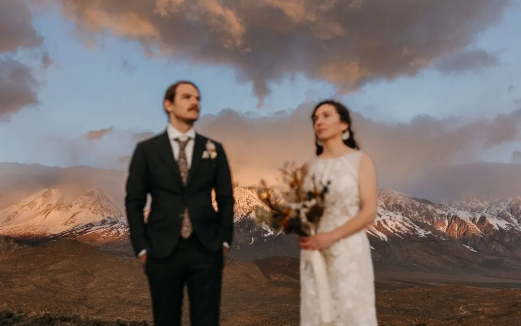 A photo of the colorful sunrise in the mountains as the eloping couple stands in the foreground.