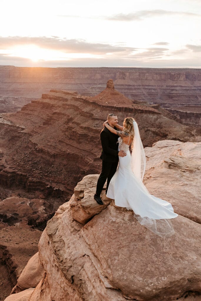 A bride and groom stand together at Dead Horse Point at Sunset