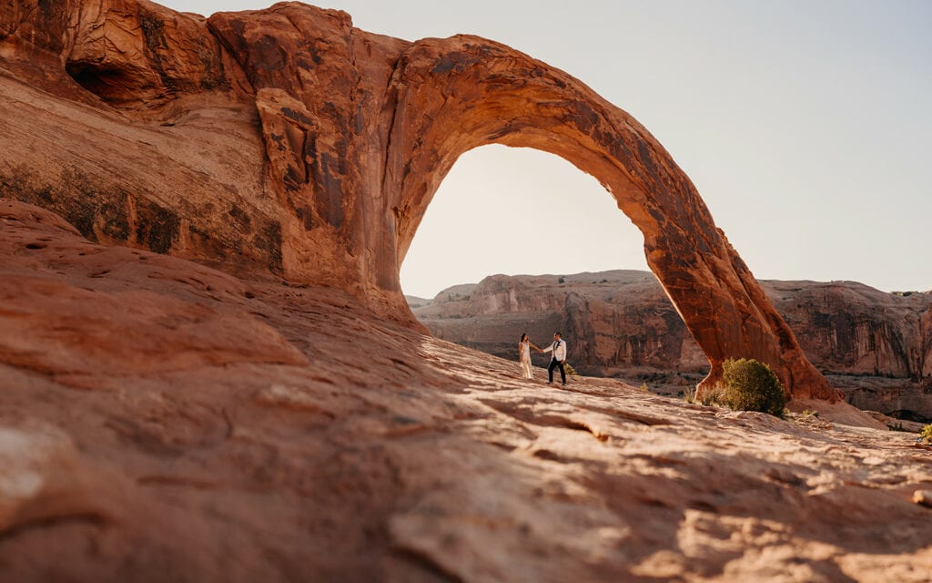 A beautiful image of the couple standing under the massive arch as the morning light shines behind them.