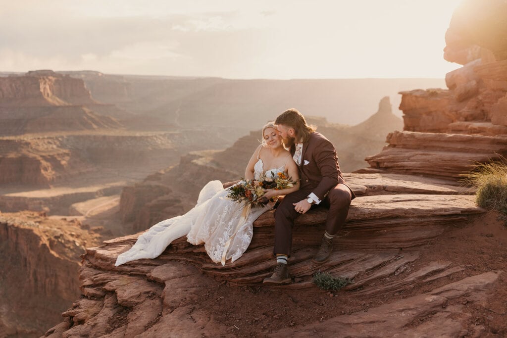 A bride and groom sit together at Dead Horse Point at Sunset
