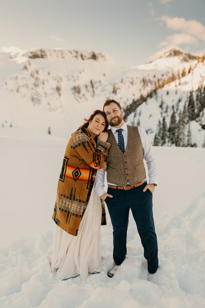 A bride and groom hold each other and smile at the camera in the snow.