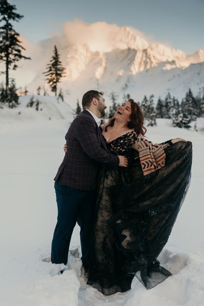 A bride and groom play together in the snow in the mountains. 