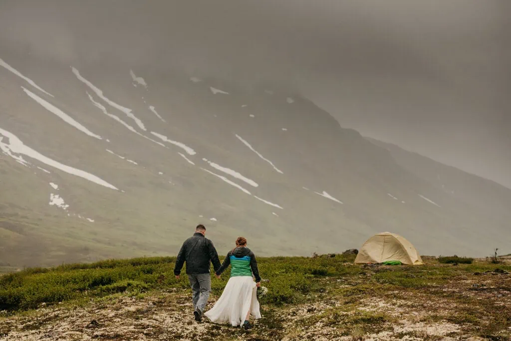 A couple holds hands and walks towards their tent on their wedding night.