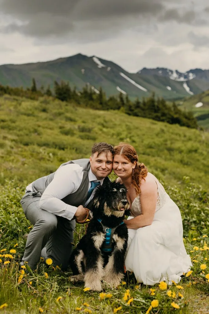The bride and groom take a photo with their dog in the flowers.
