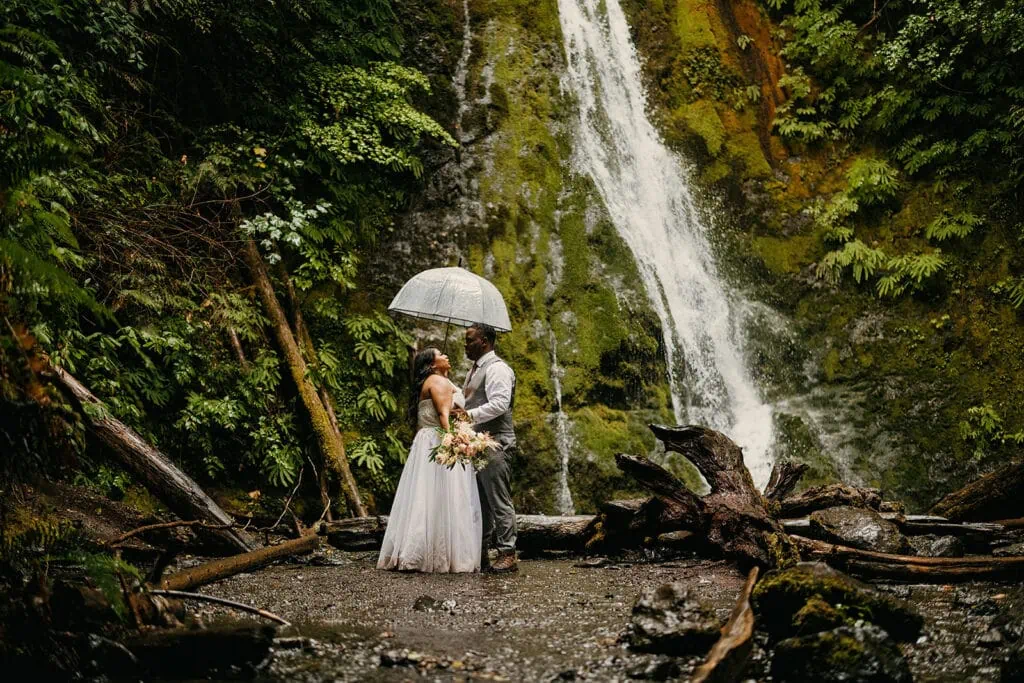 A couple gathers under an umbrella by a waterfall in Olympic National Park.