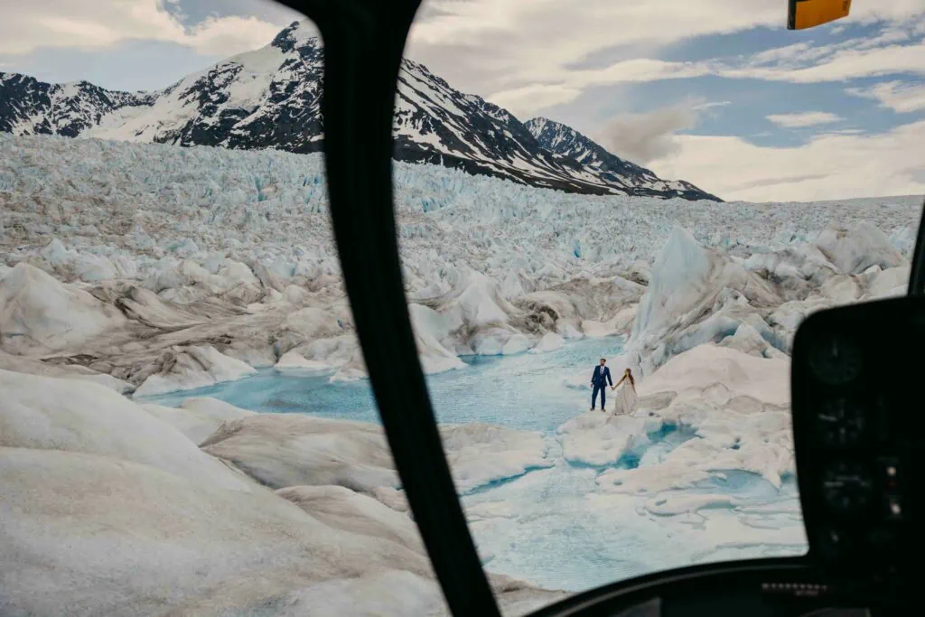 A couple explores a glacier as the photographer takes a photo from inside the helicopter.