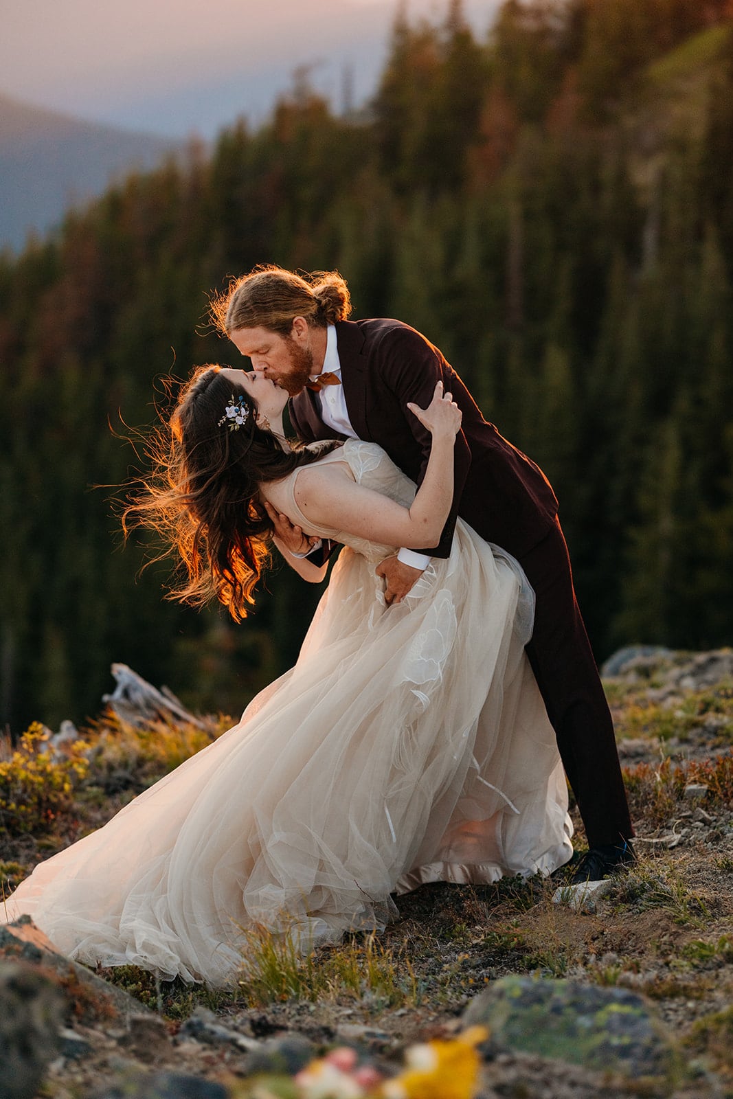 A couple shares a dip kiss in the red glowing sunset light on the mountain.