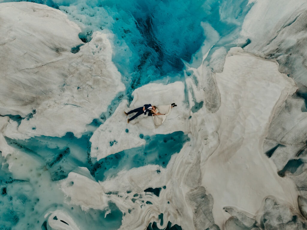 A couple lays on an iceberg surrounded by a glacier pool. 