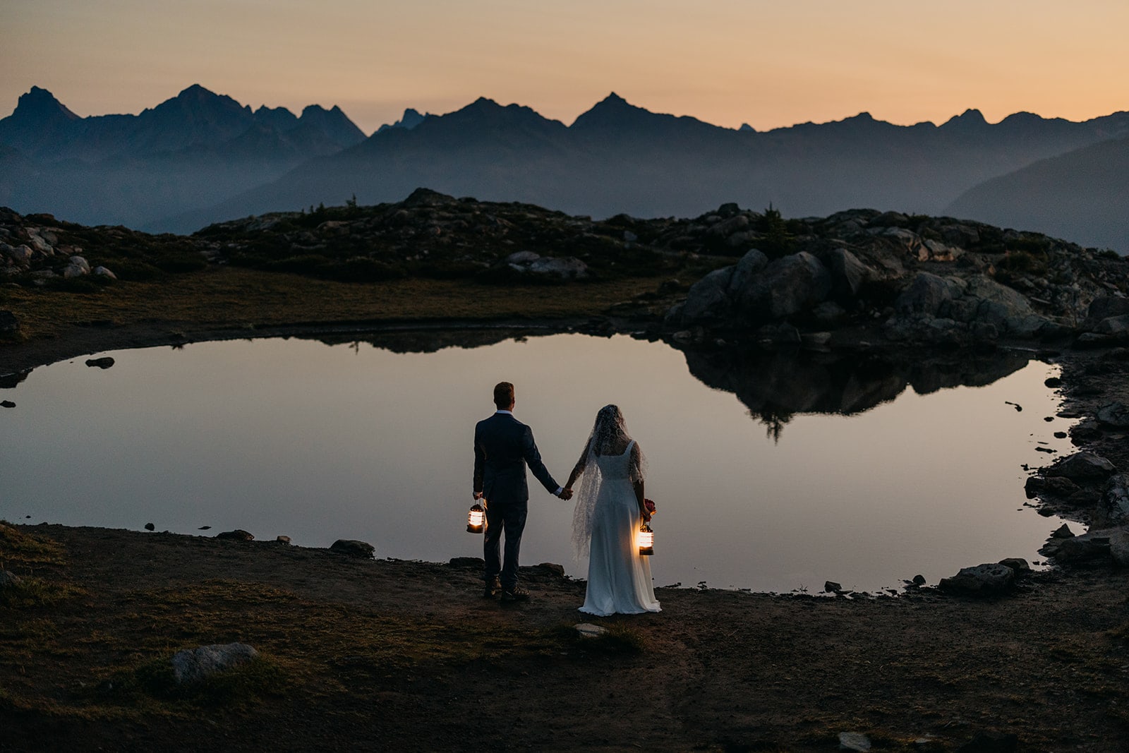 The couple stands at a lake before sunrise.