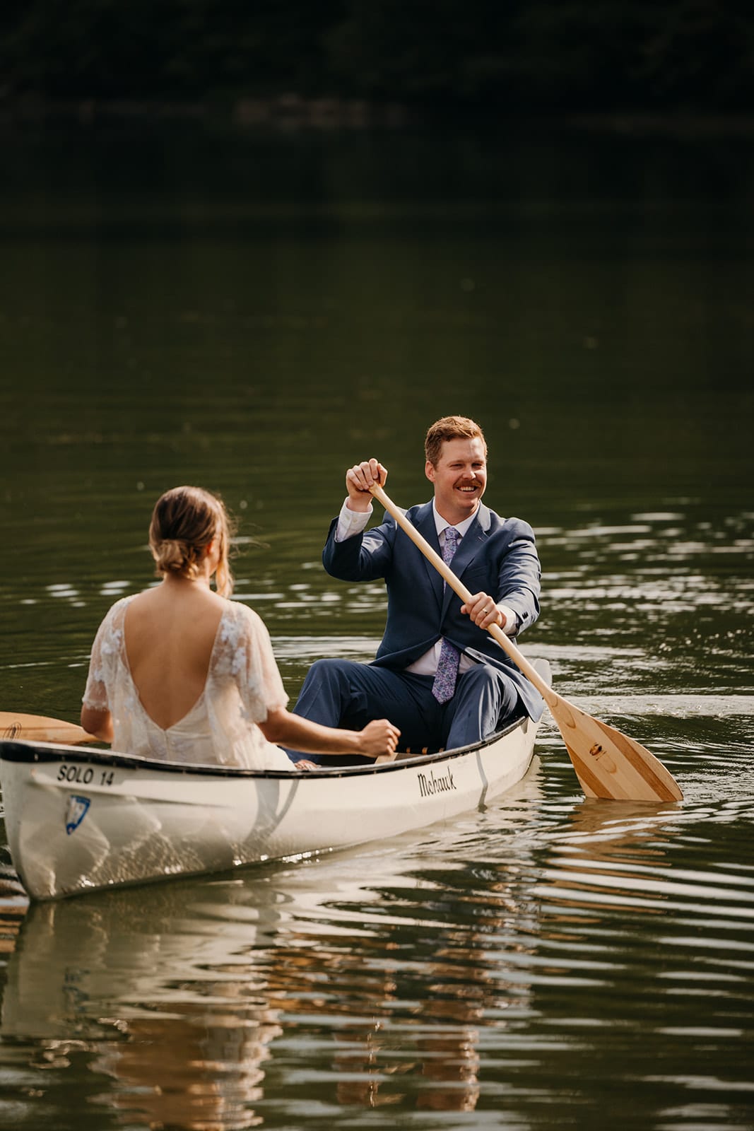 The groom paddles a canoe on the lake at camp.