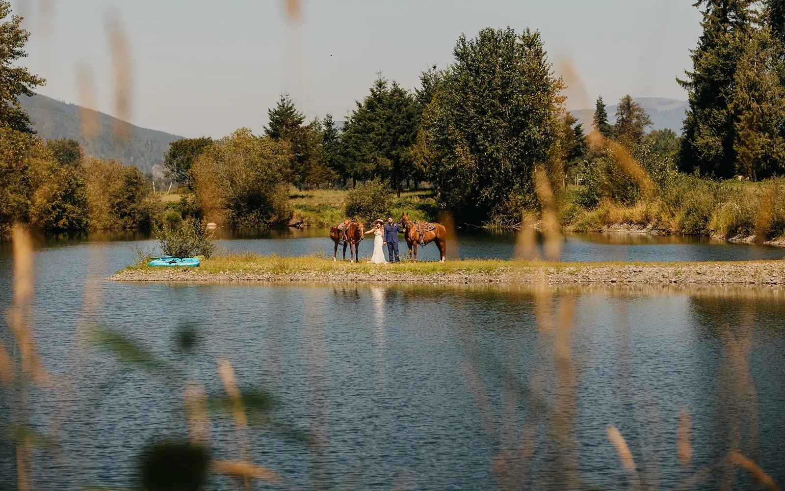 The couple stands with horses by the pond. 