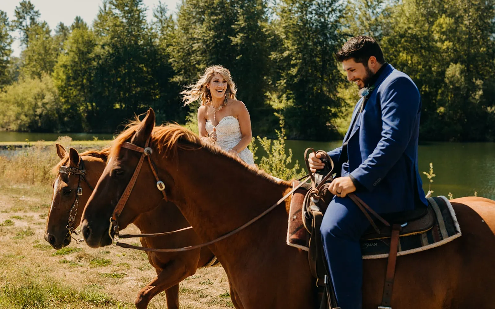 A bride smiles at her groom as they ride horse back together on a summer day.