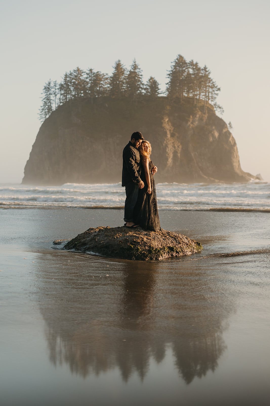 A couple stands together on a rock in Olympic National Park. 