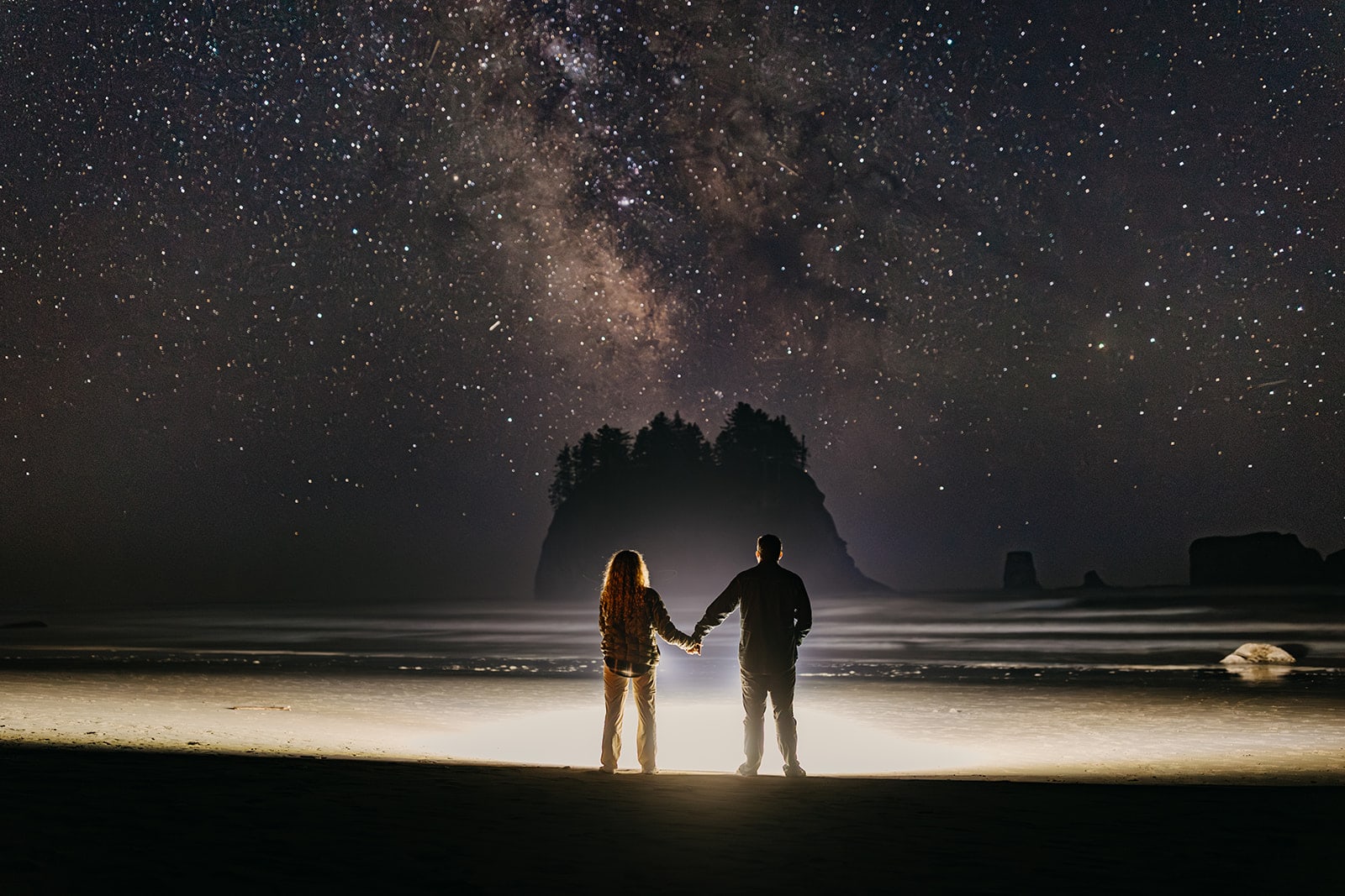 A couple looks at the milky way on the coast. 