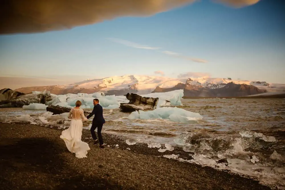 A bride and groom run together among the ice fields and black sand beaches of Iceland.