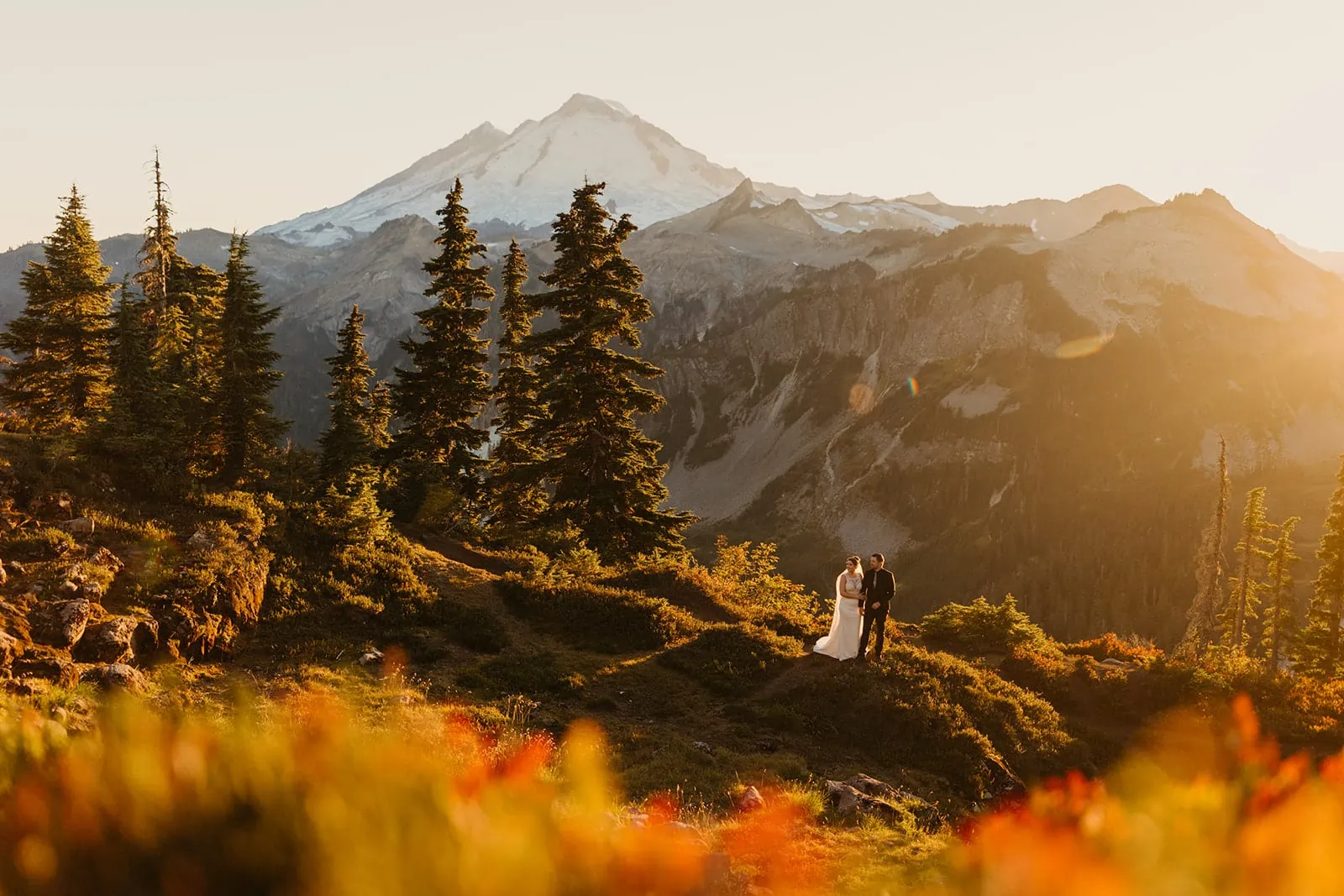 A couple stands in the distance with a fall sunset mountain landscape.