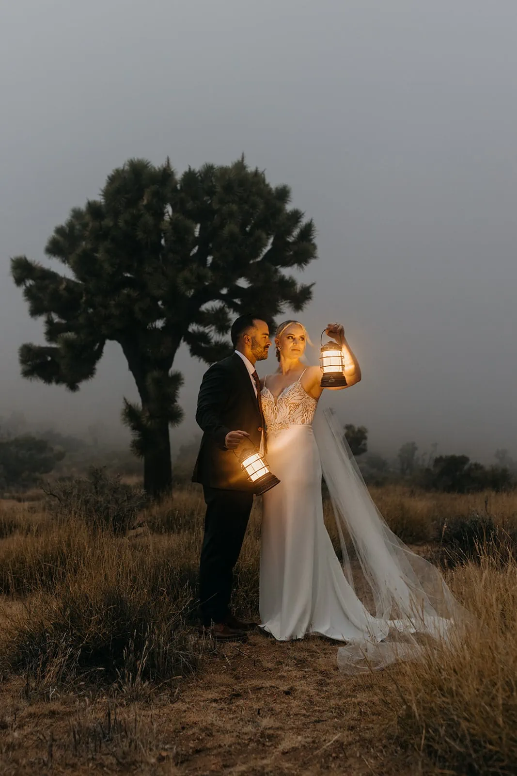 A couple stands in Joshua Tree on a moody evening holding lanterns.