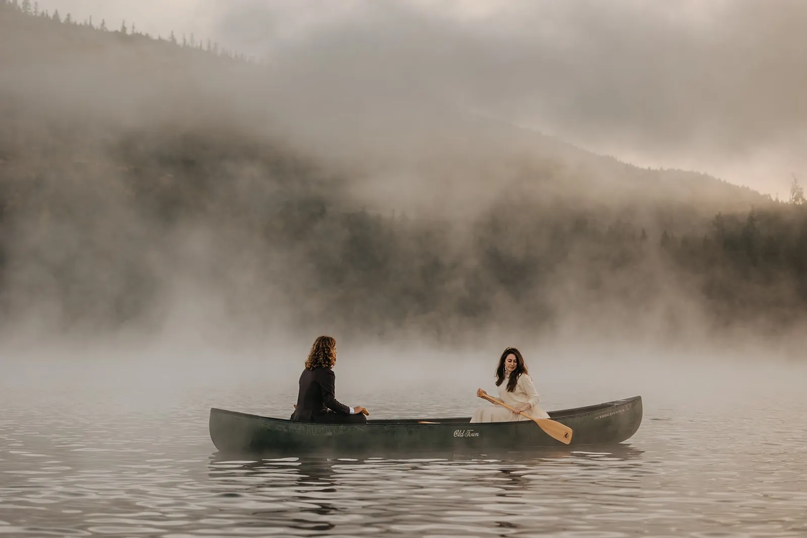 A couple canoes on a lake on a foggy morning to start off their wedding day.