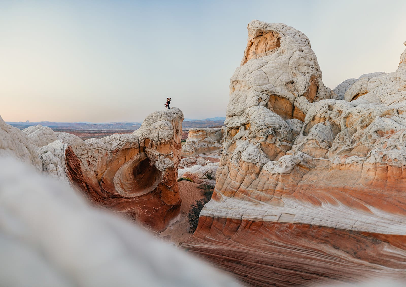 A couple stands on top of a beautiful rock formation at dusk.